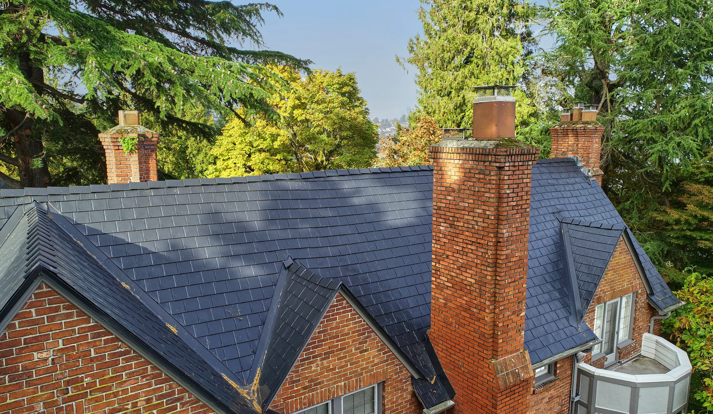 Black Interlock Slate aluminum roof on a red brick house with a metal roof in a forested area, Seattle, Washington