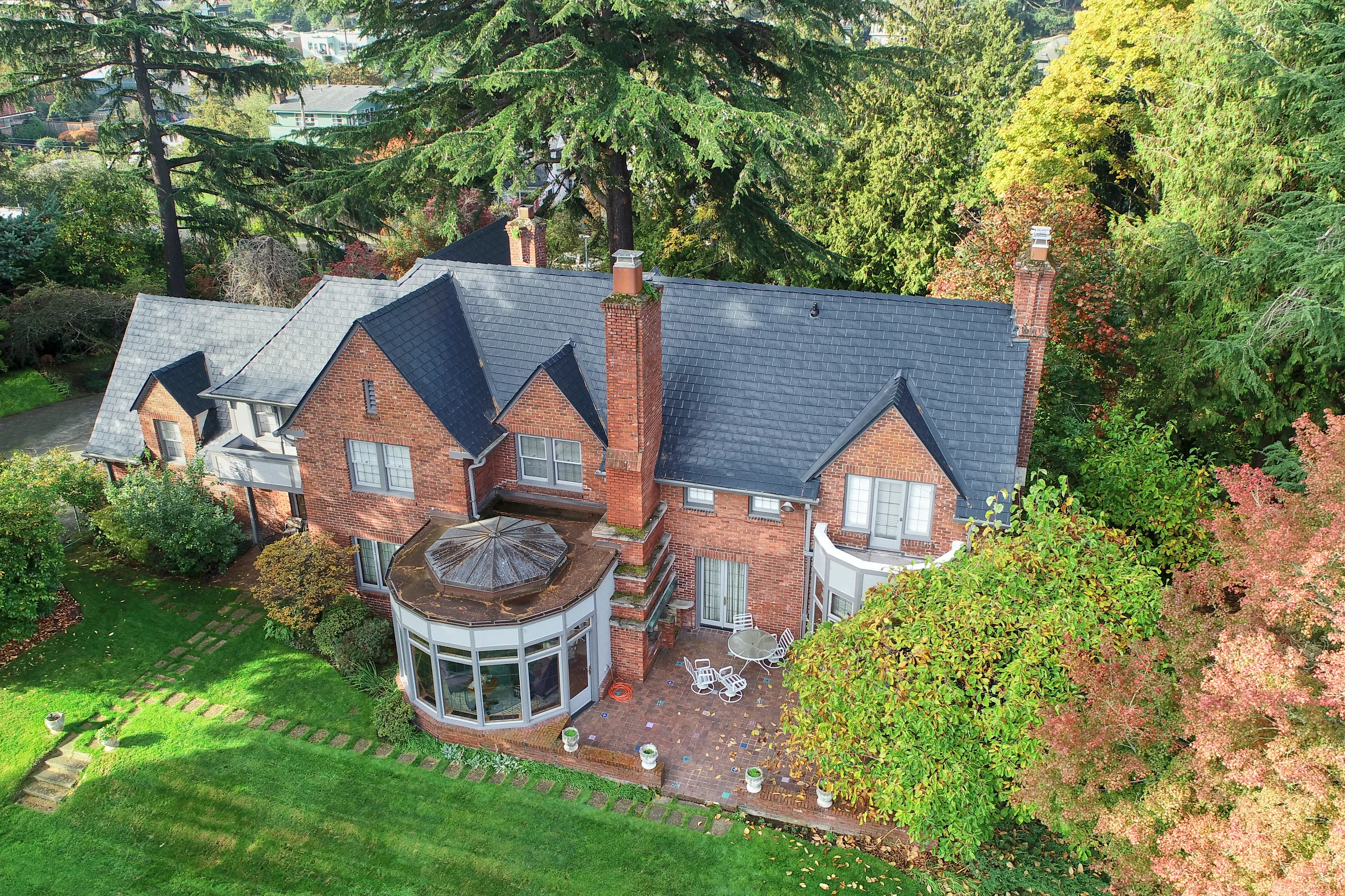 Black Interlock Slate aluminum roof on a red brick Tudor home with dormers among tall green trees, Seattle, Washington