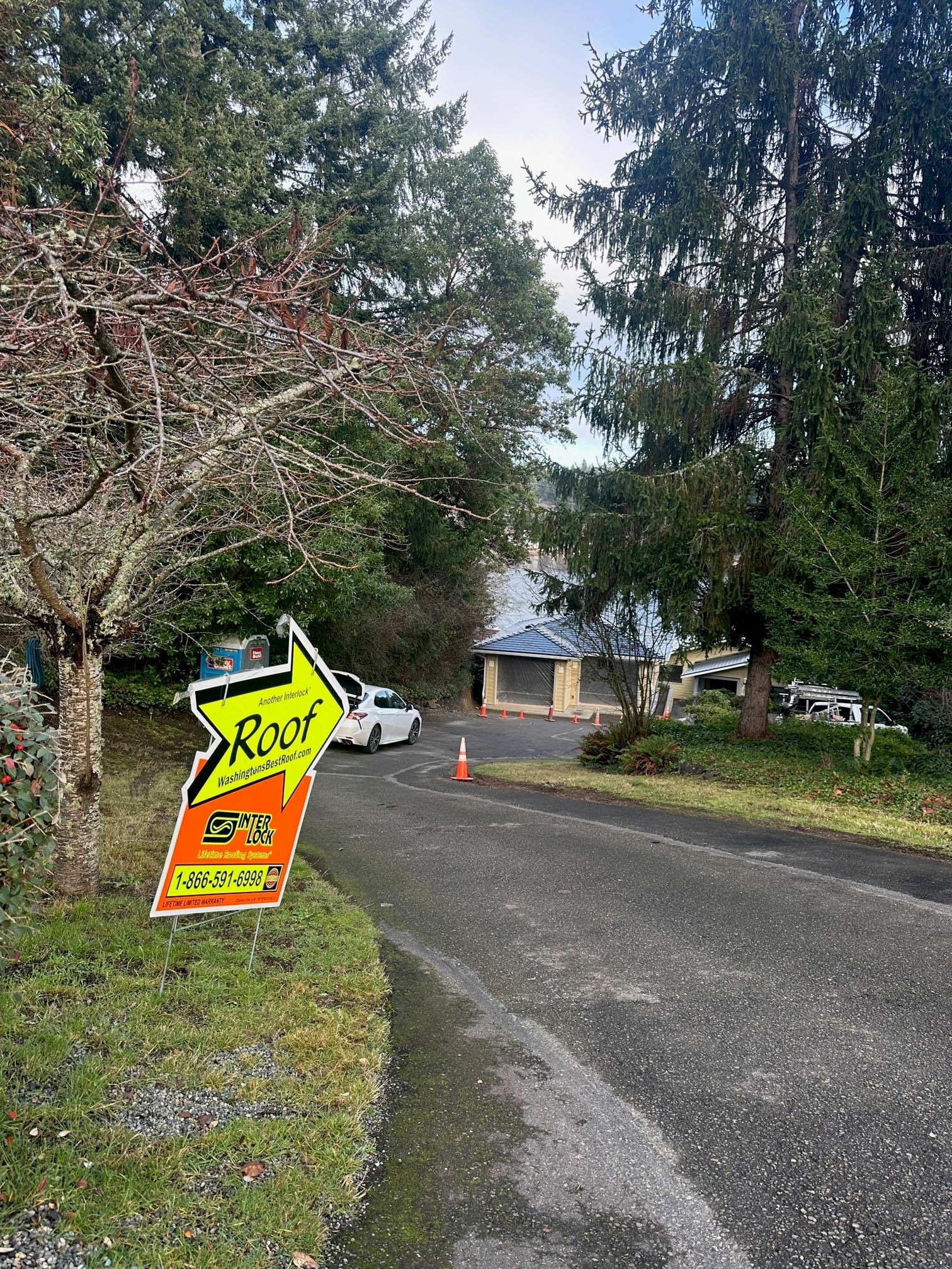 Street-view of a single-family home in Lakewood WA with a newly installed black Interlock aluminum cedar shingle metal roof, framed by tall evergreens.