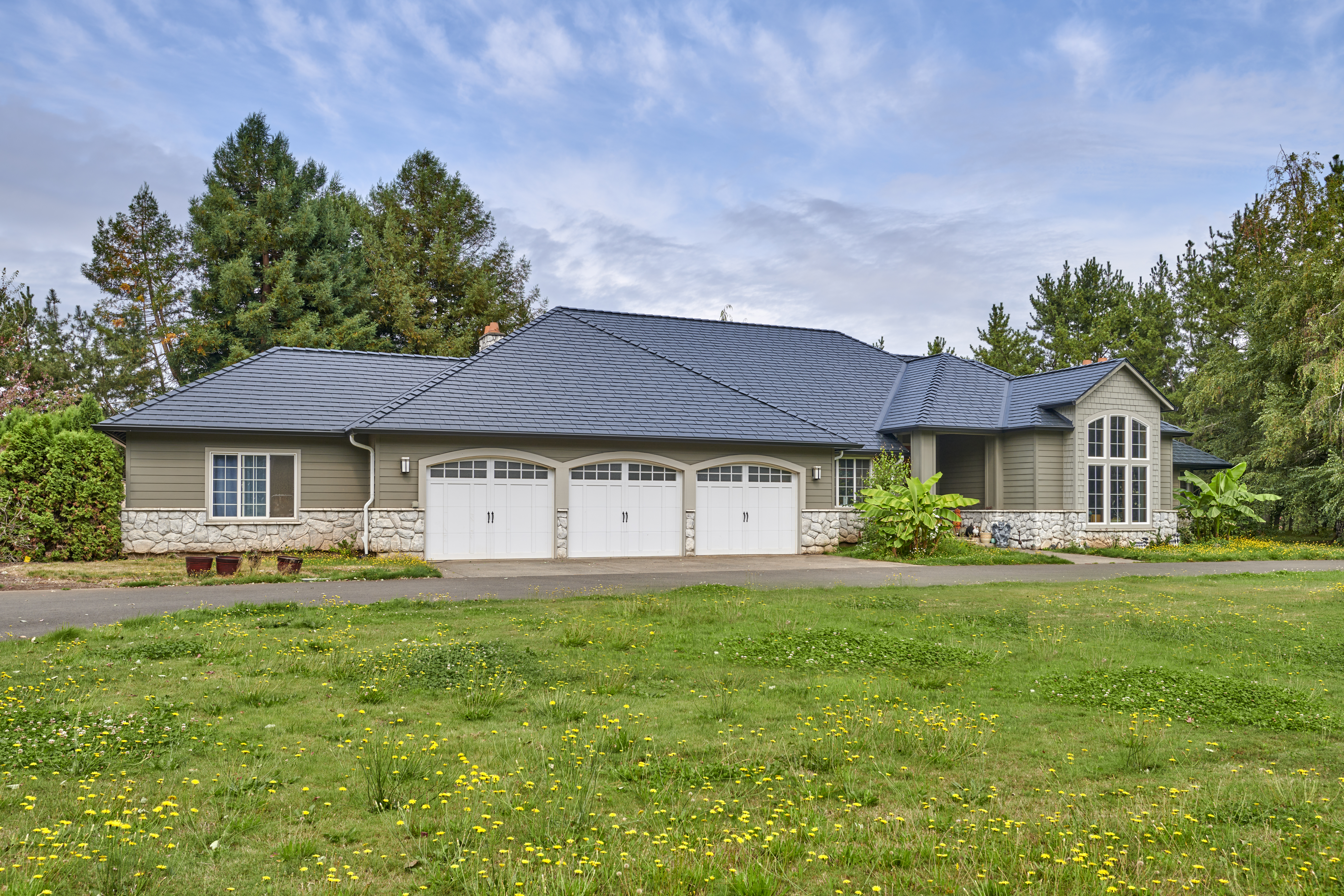Single-family ranch home with Interlock black aluminum slate metal roofing, multi-hip complex roof, three-car garage, and stone accents in Ridgefield, WA.