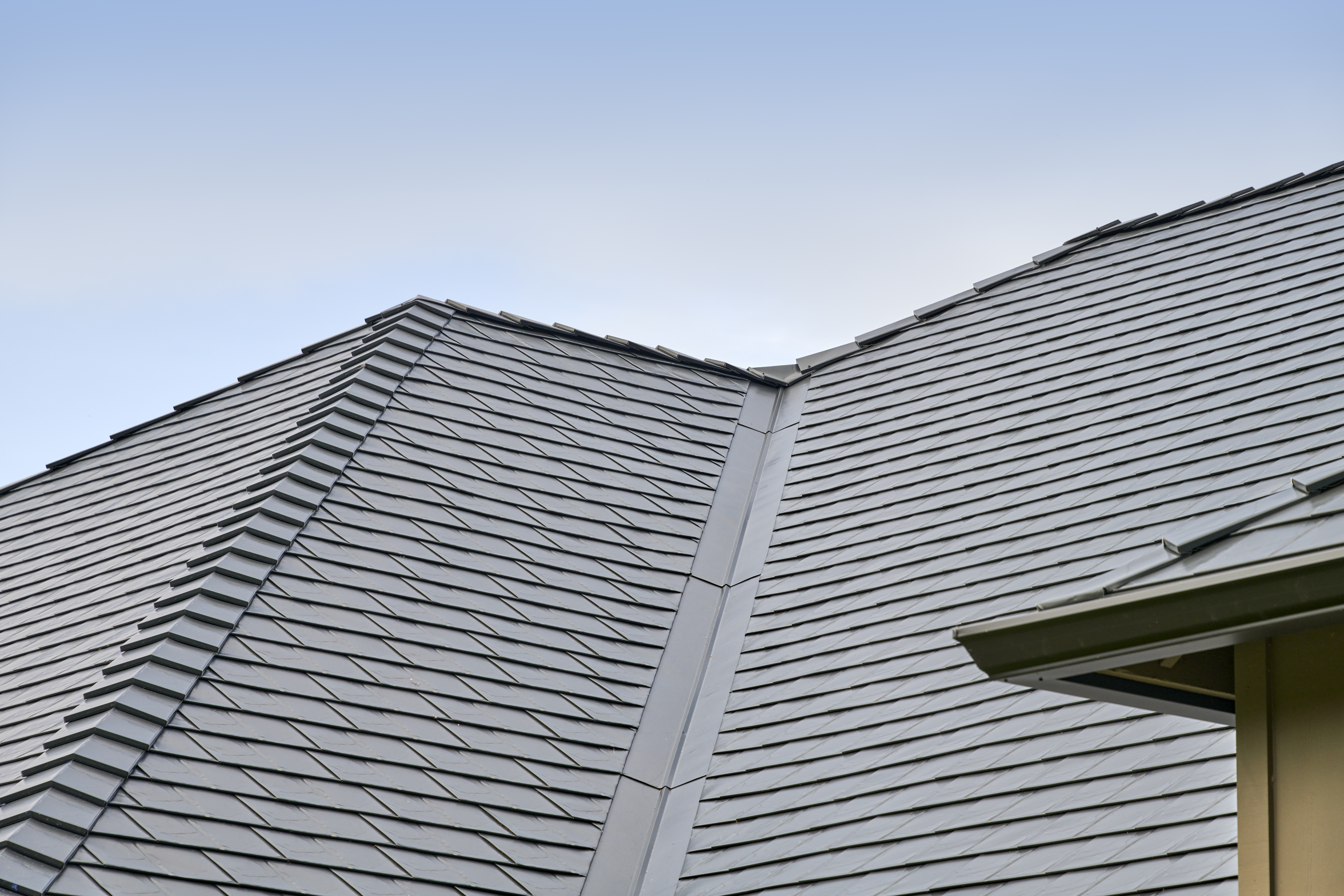 Close-up of dark grey Interlock aluminum slate metal roofing showing a valley intersection and hip ridges under a clear blue sky.