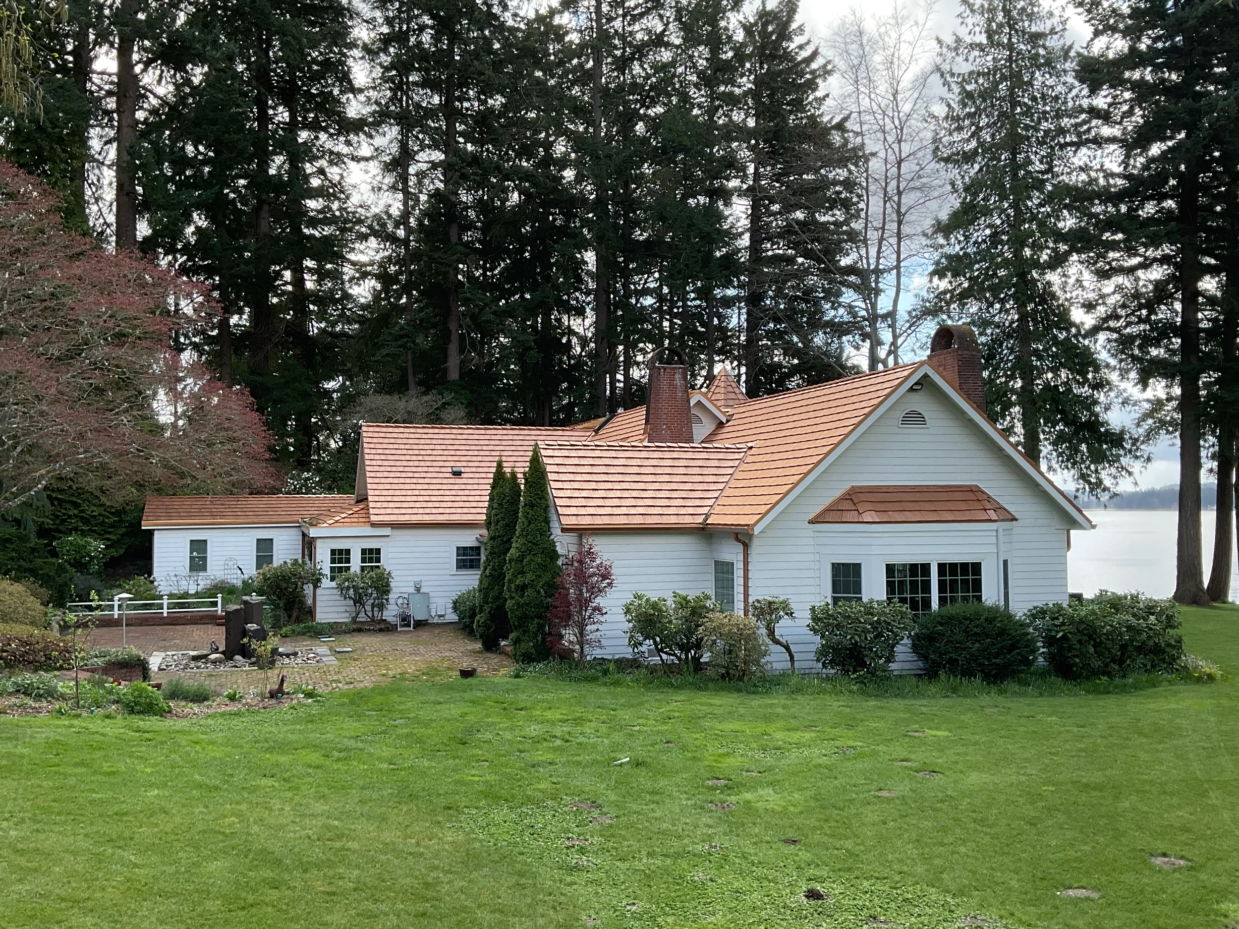 Copper Penny Interlock Shake aluminum roof on a white cottage among tall evergreens on the water, Bremerton, Washington