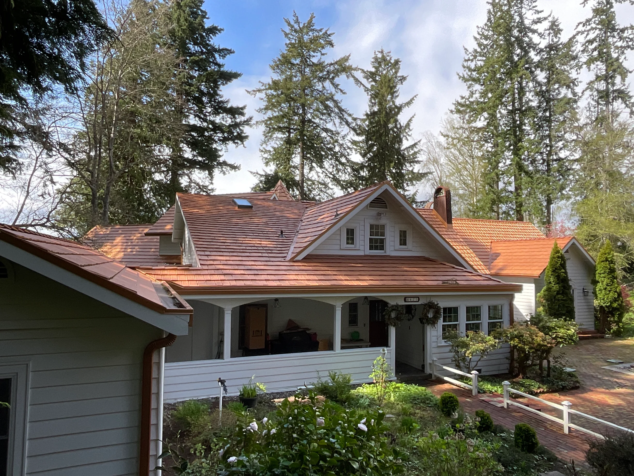Copper Penny Interlock Shake aluminum roof on a cream two-storey Craftsman home with dormers among tall, Bremerton, Washington
