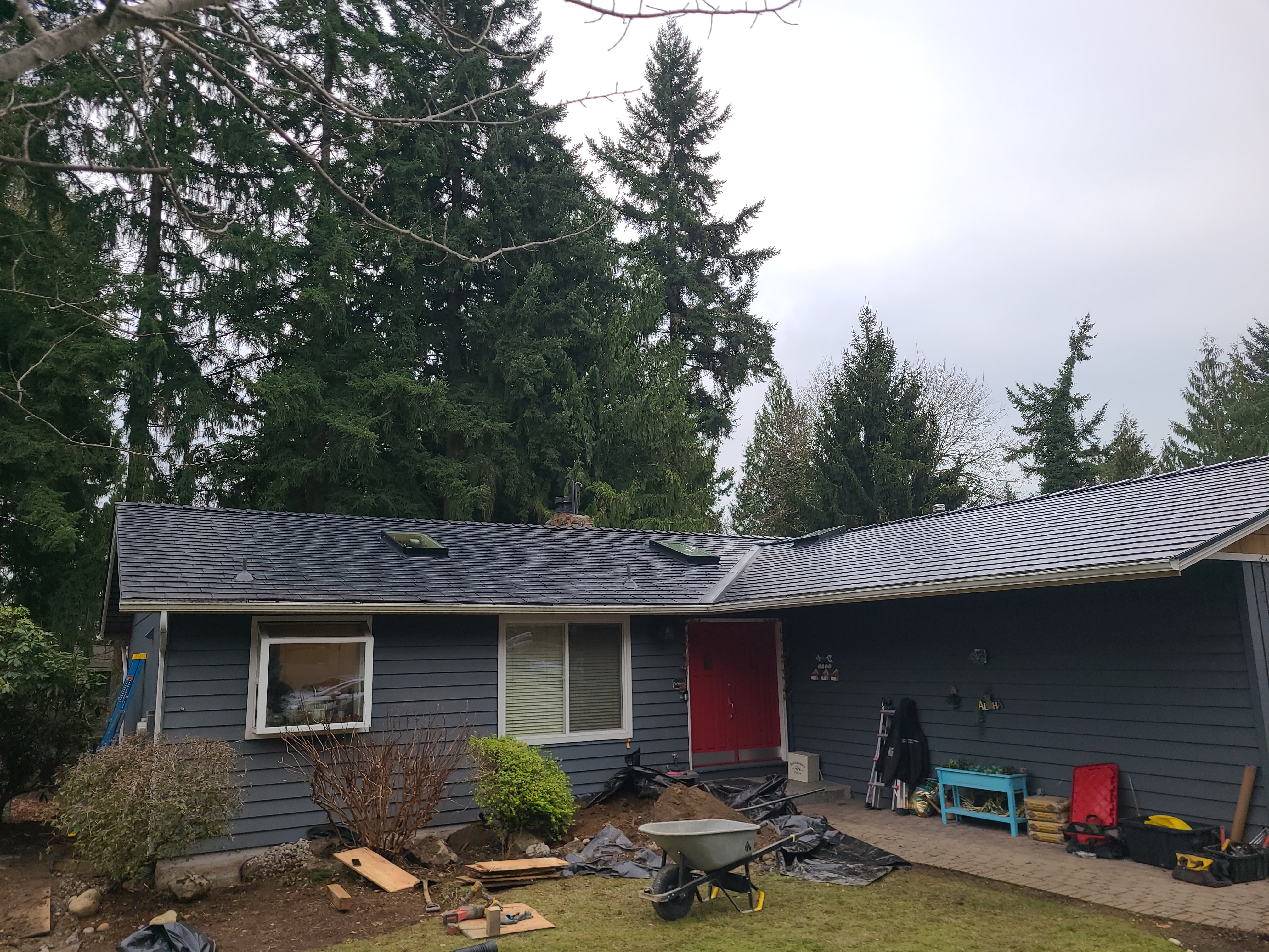 Front elevation of a gray ranch home with a newly installed Interlock black aluminum slate metal roof, skylights, and red front door in Redmond, WA.