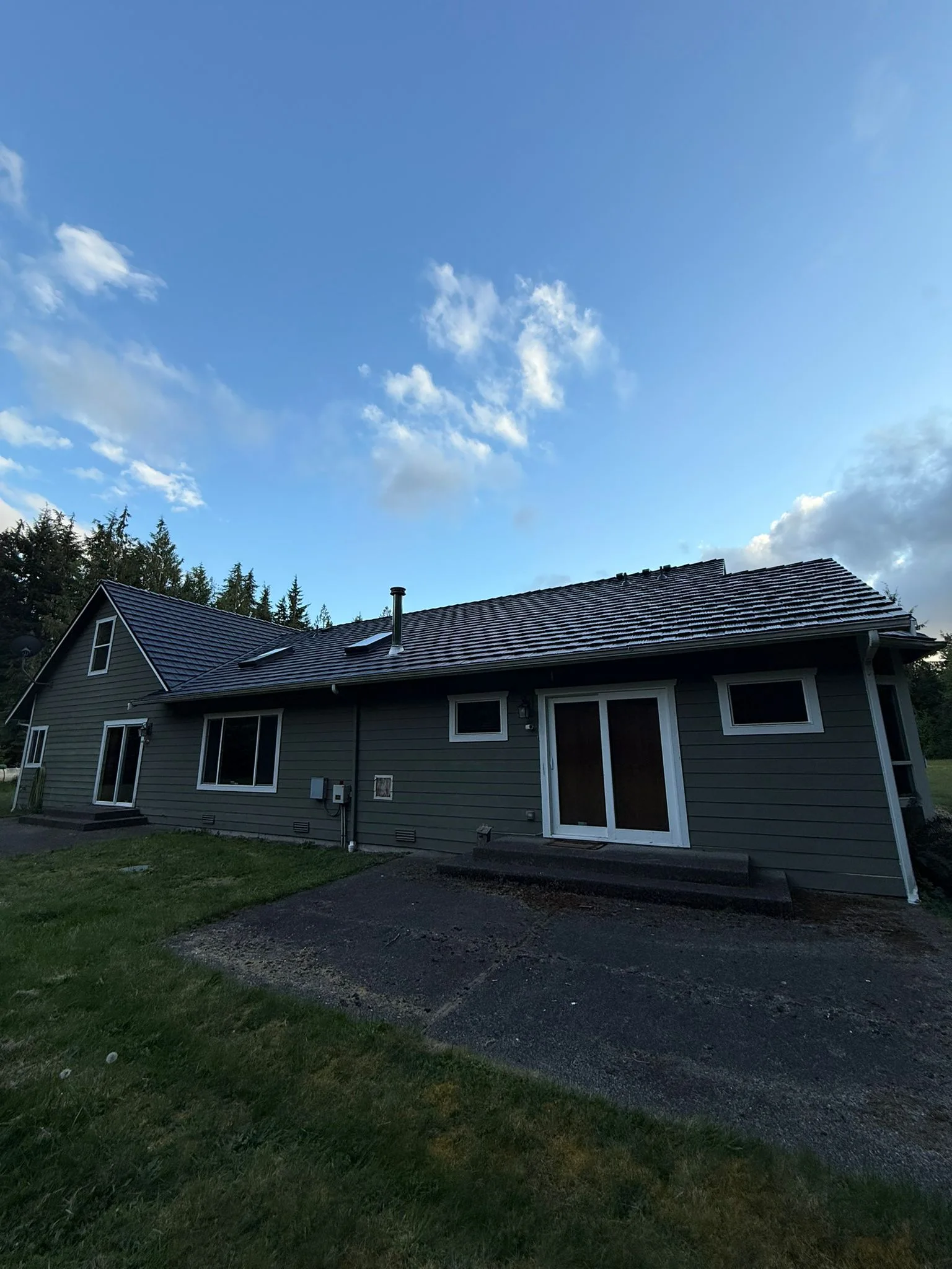 Black Interlock Shake aluminum roof on a green single-storey home with a metal roof among tall, Marysville, Washington