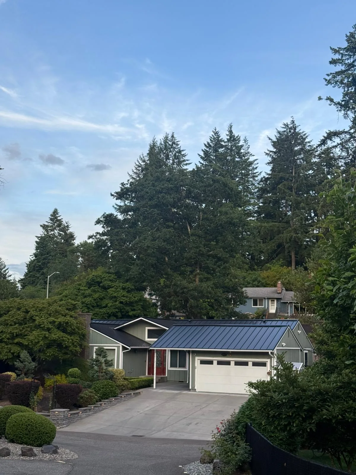 Black Interlock Standing Seam aluminum roof on a grey two-storey home with dormers among tall pines, Lakewood, Washington