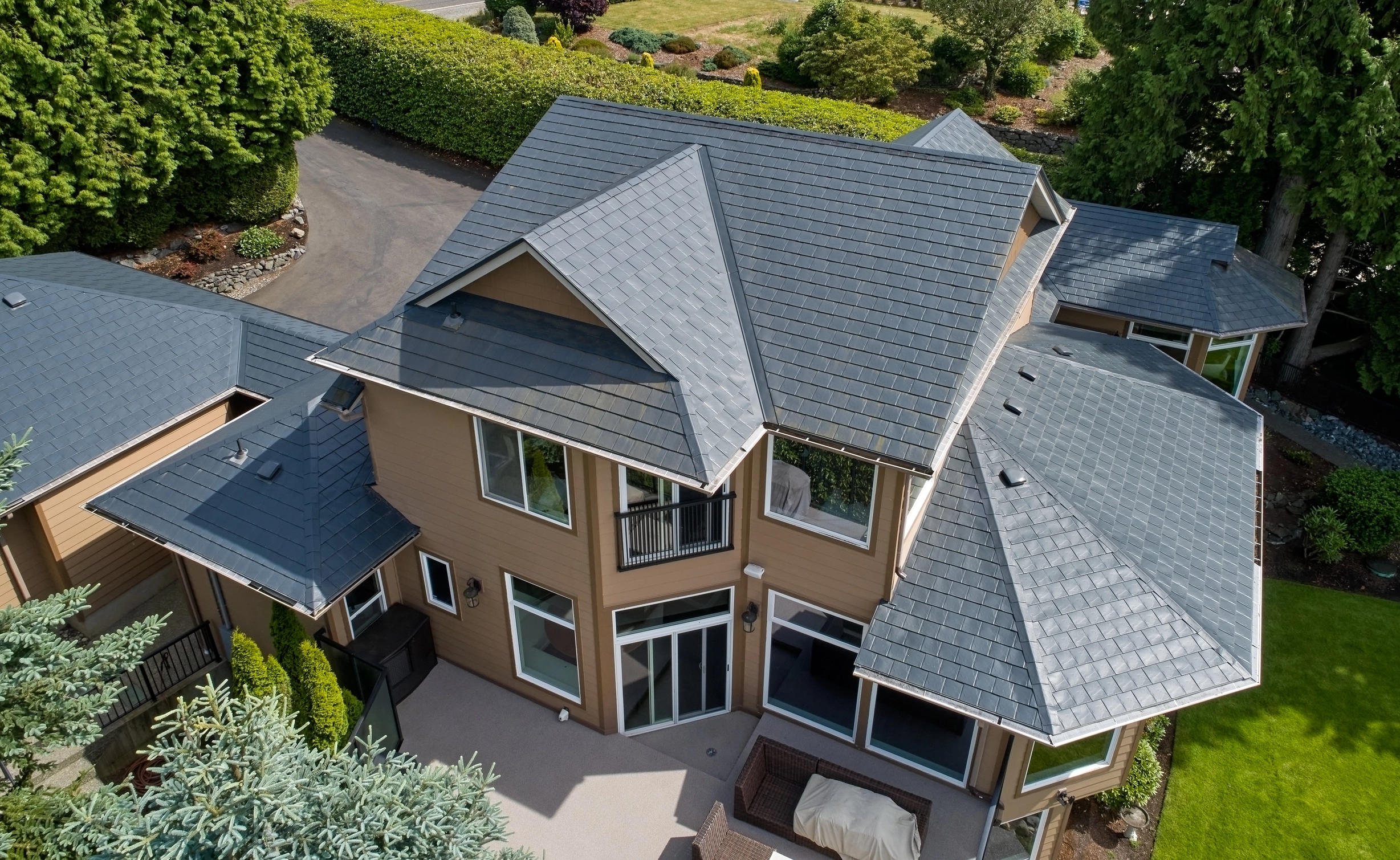 Deep Charcoal Interlock Slate aluminum roof on a tan two-storey home with dormers among tall trees, Blaine, Washington