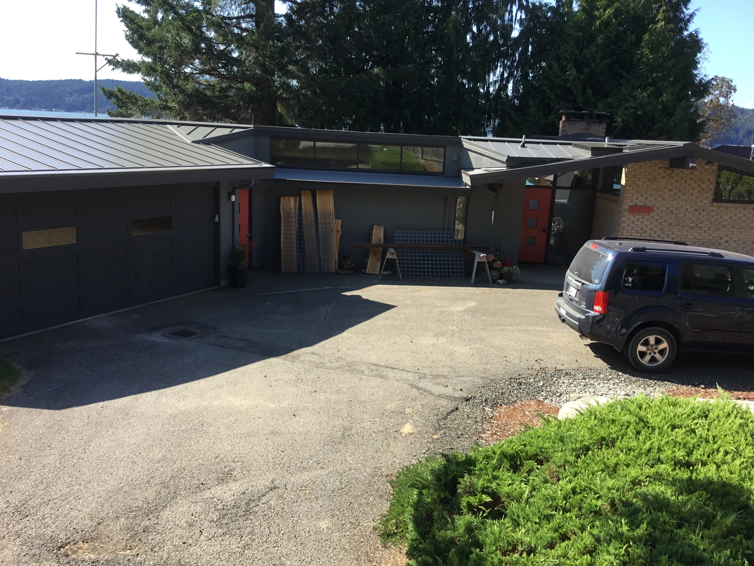 Musket Grey Interlock Standing Seam aluminum roof on a two-storey modern home with a metal roof among tall pines, Belfair, Washington