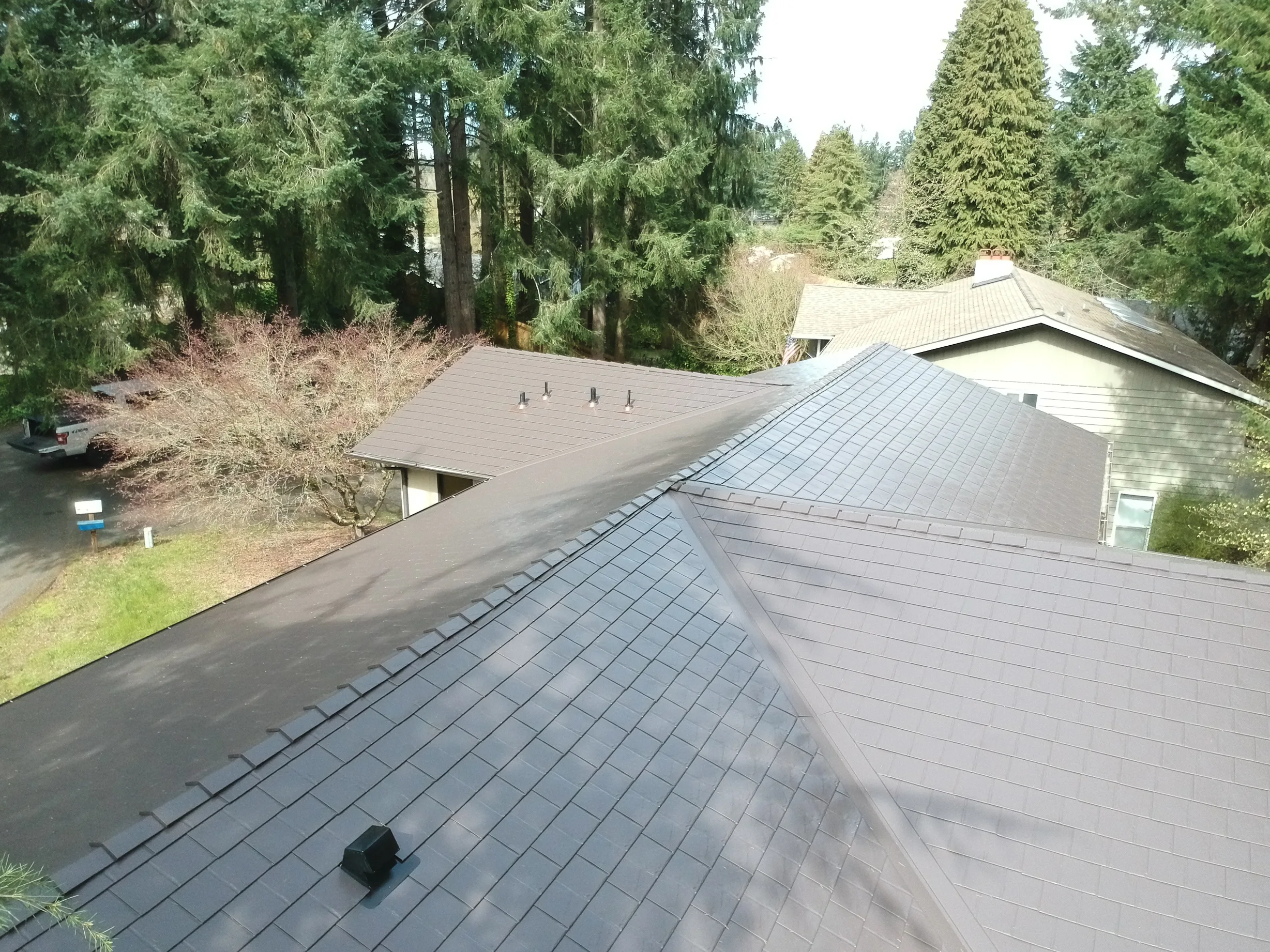 Tudor Brown Interlock Slate aluminum roof on a two-storey home with a metal roof among tall evergreen, University Place, Washington