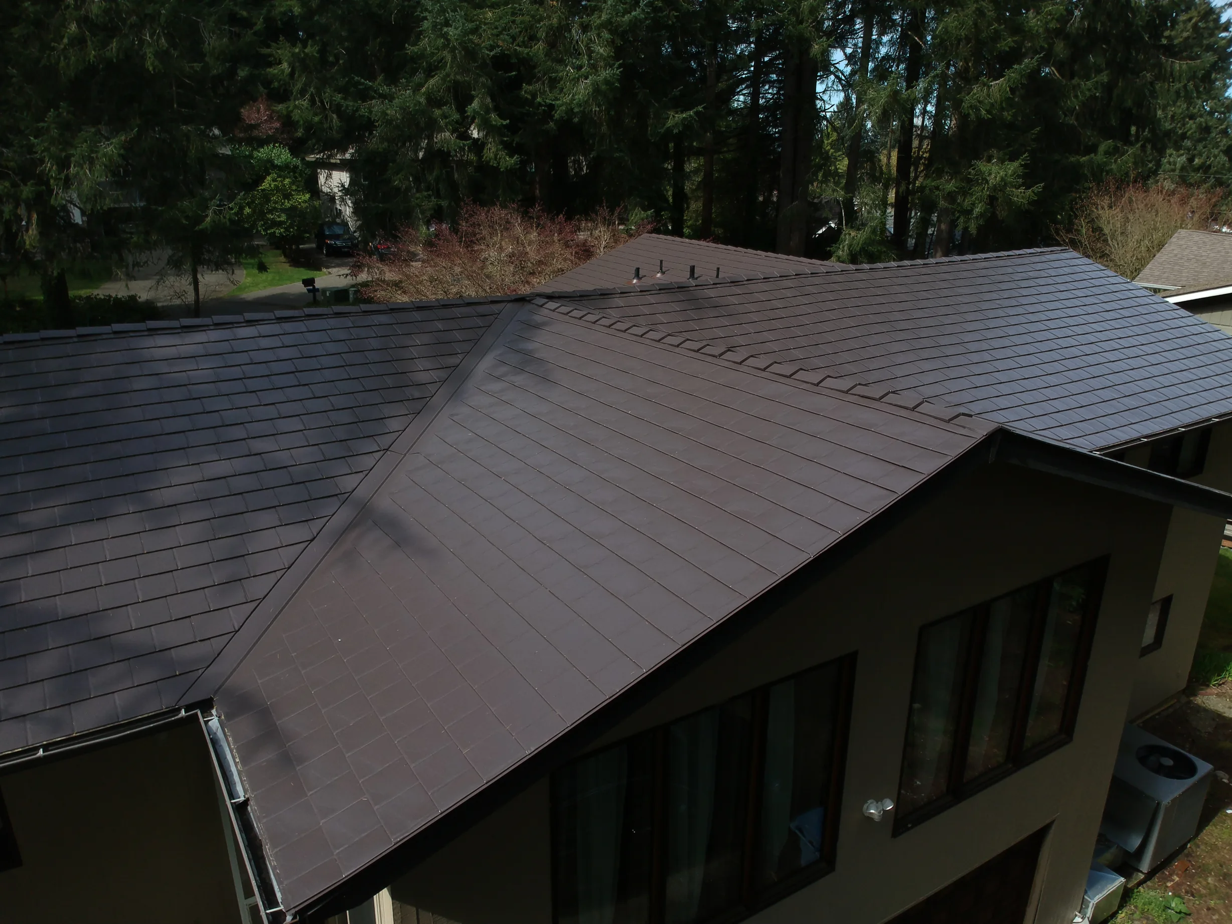 Tudor Brown Interlock Slate aluminum roof on a brown two-storey home with dormers among tall pines, University Place, Washington