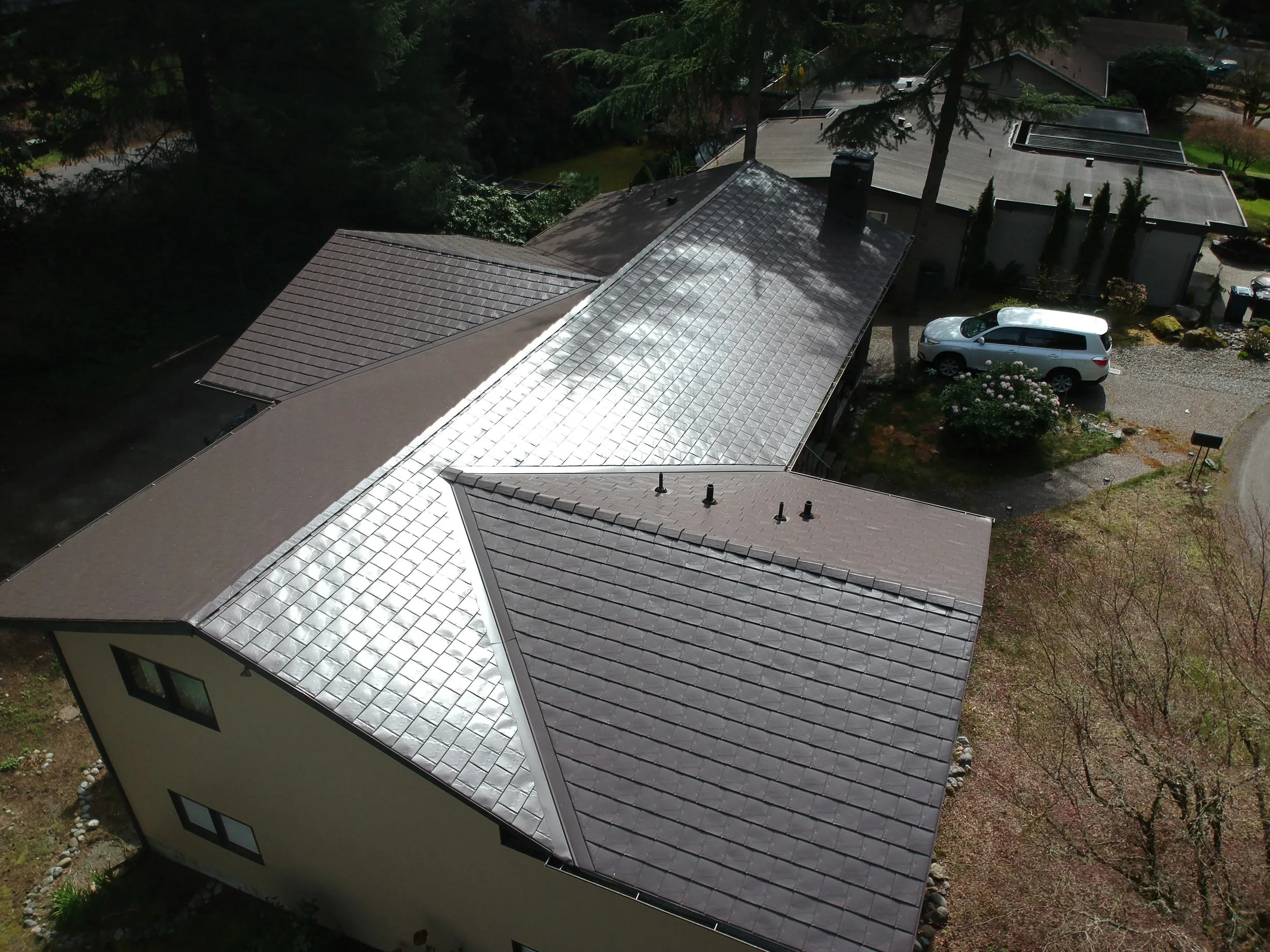 Tudor Brown Interlock Slate aluminum roof on a beige Tudor home with dormers in a forested setting, University Place, Washington