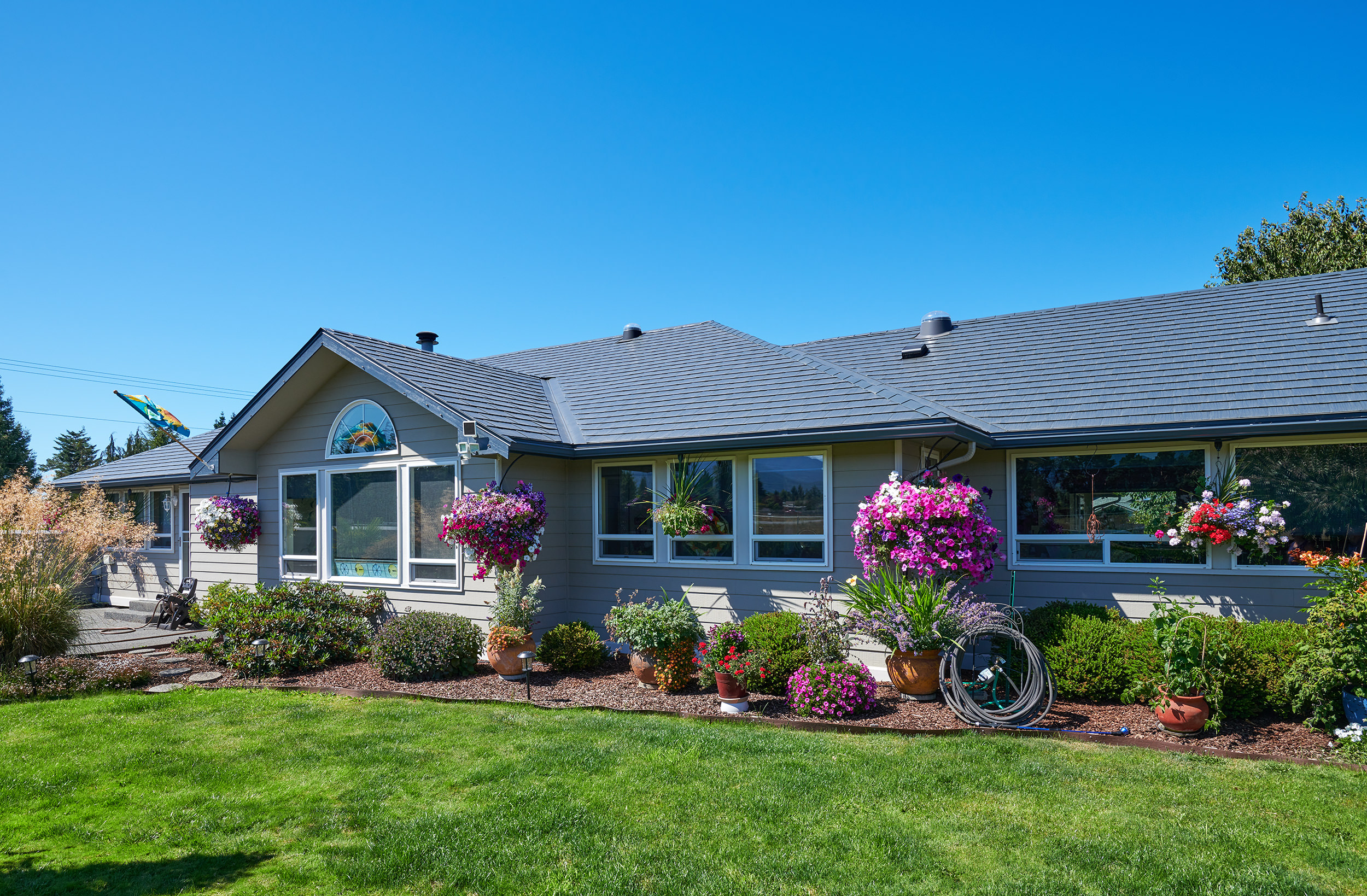 Single-story ranch home in Sequim, WA with Interlock deep charcoal aluminum slate metal roofing, multi-hip profile, and lush hanging flower baskets.