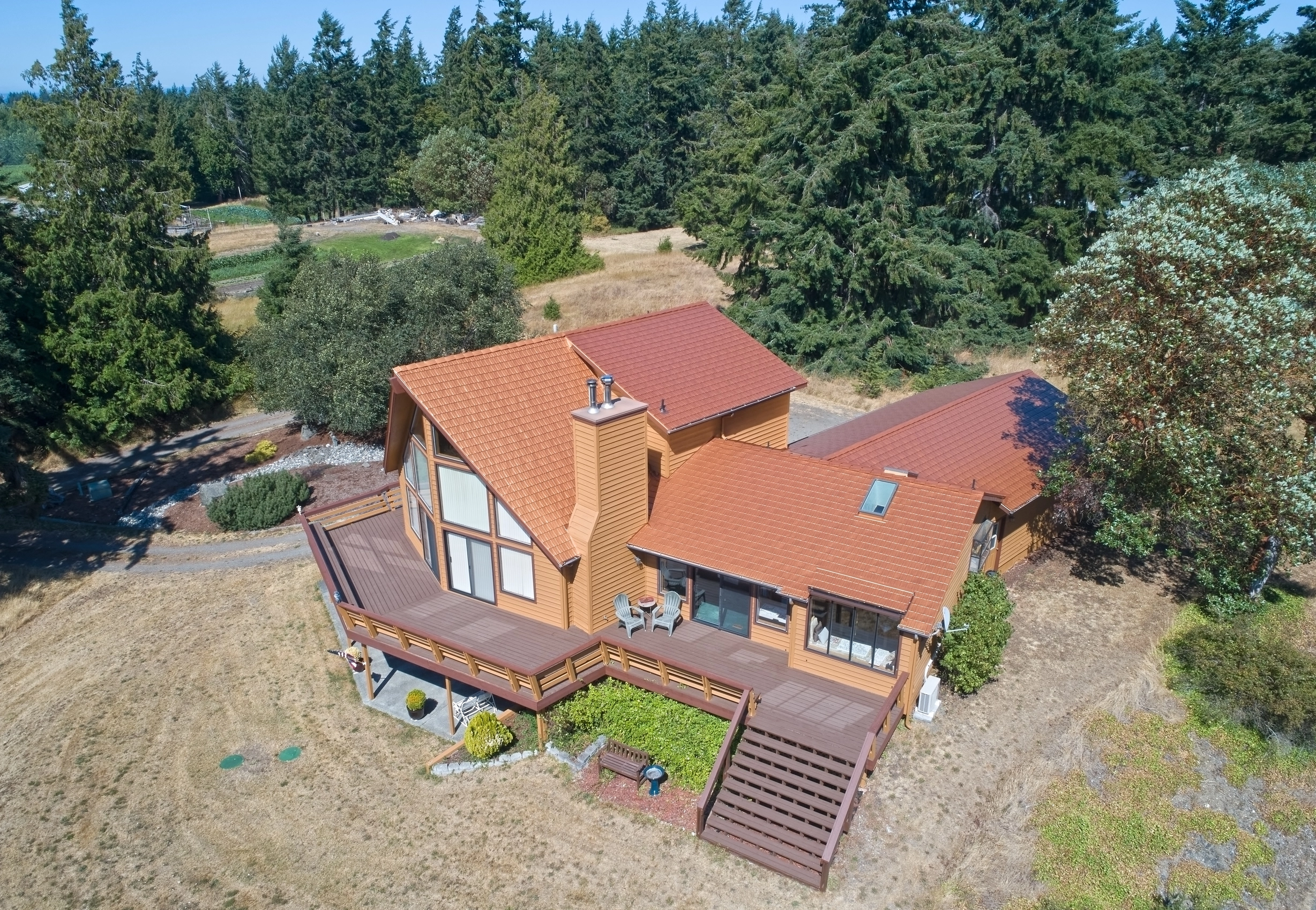 Copper Penny Interlock Cedar Shingle aluminum roof on a two-storey home with a brown metal roof among tall pines, Sequim, Washington