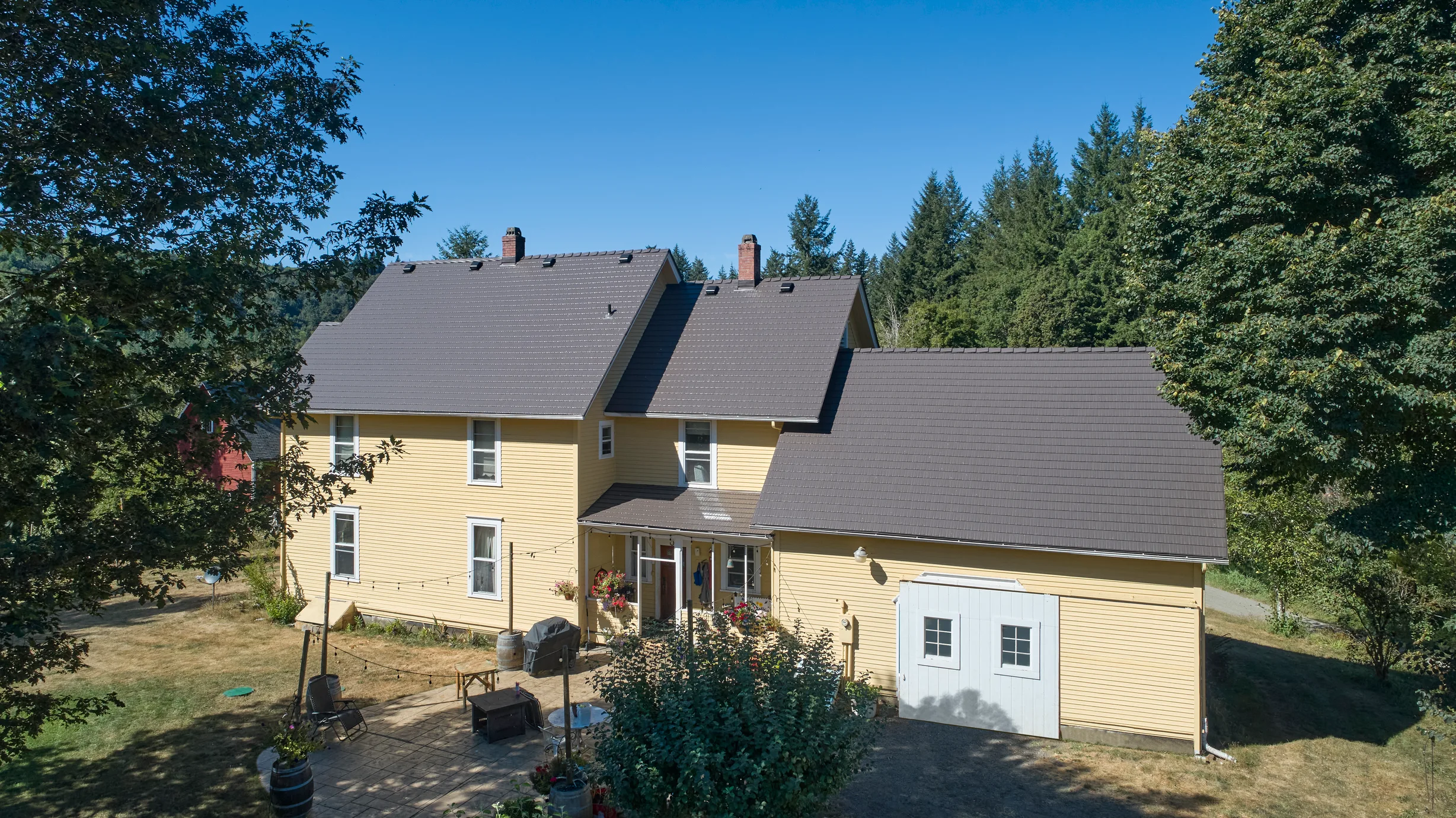 Black Interlock Slate aluminum roof on a yellow two-storey home with dormers among tall pines, Longview, Washington
