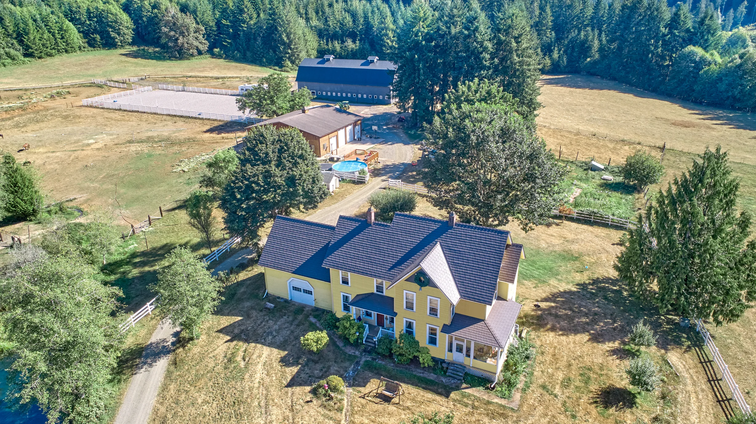 Black Interlock Slate aluminum roof on a yellow two-storey home with dormers among tall pines, Longview, Washington