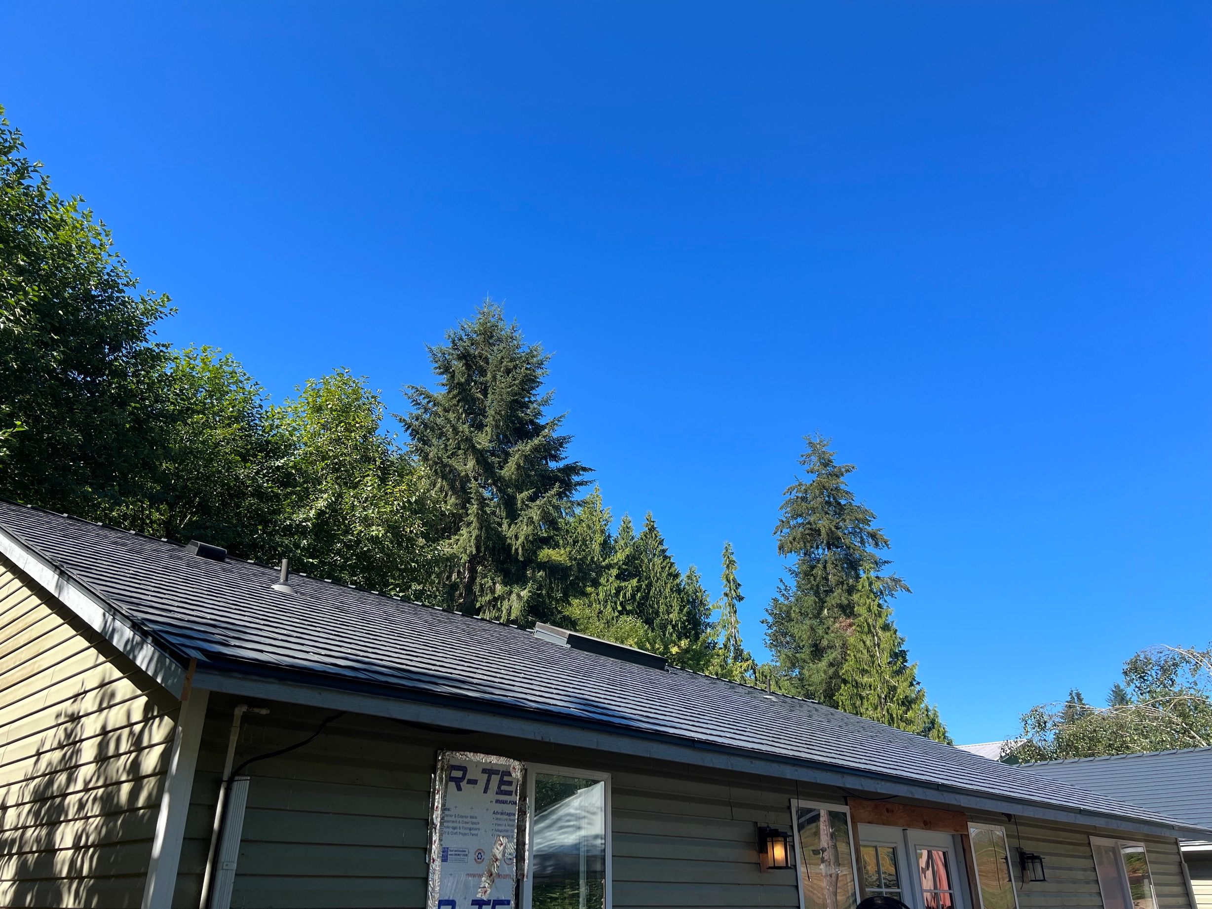 Deep Charcoal Interlock Cedar Shingle aluminum roof on a beige one-storey home with dormers among tall pines, Longview, Washington