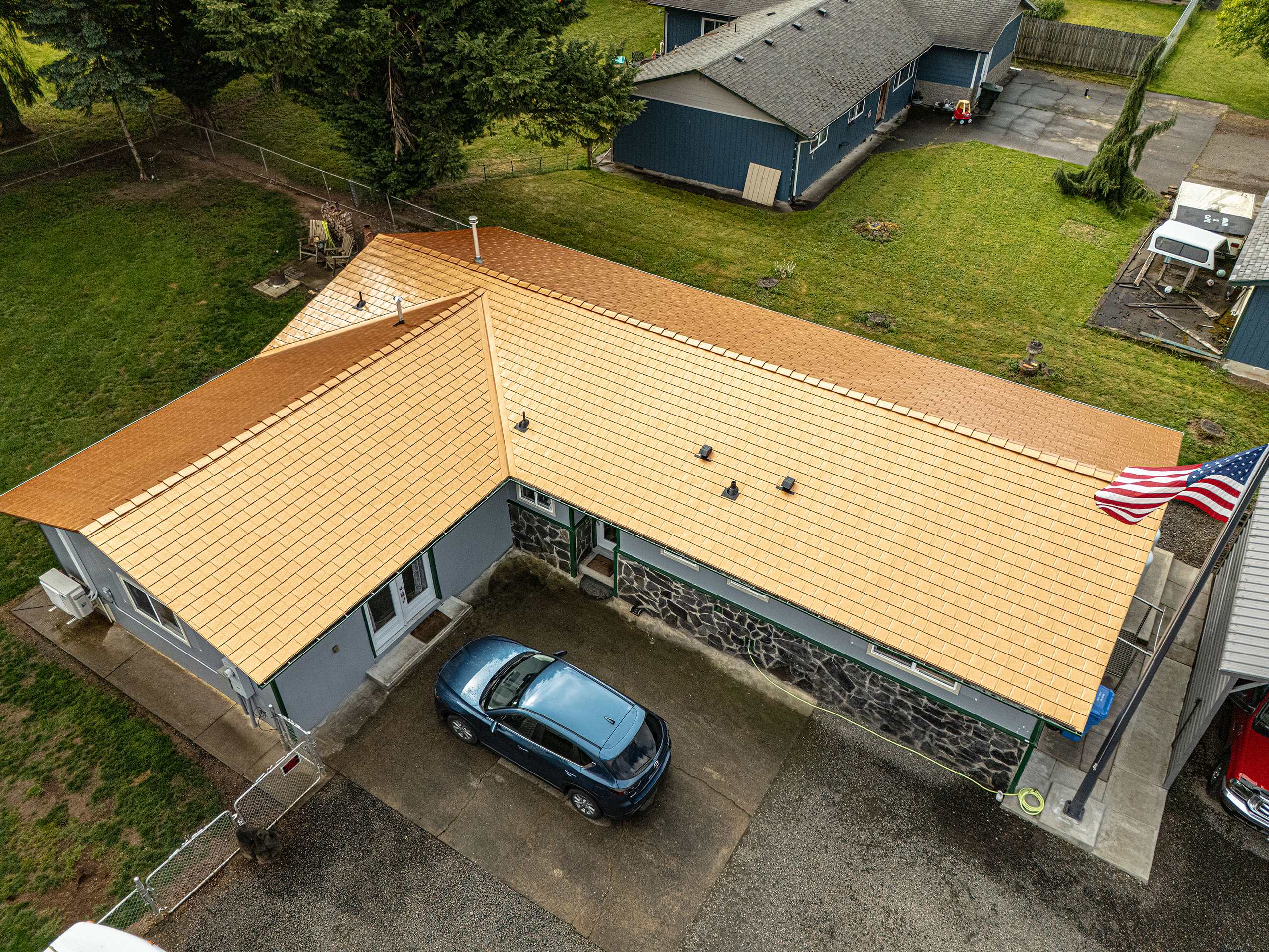 Aerial view of a single-story ranch home in Castle Rock, WA featuring a new Interlock aluminum slate roof in Copper Penny, with stone facade and American flag.