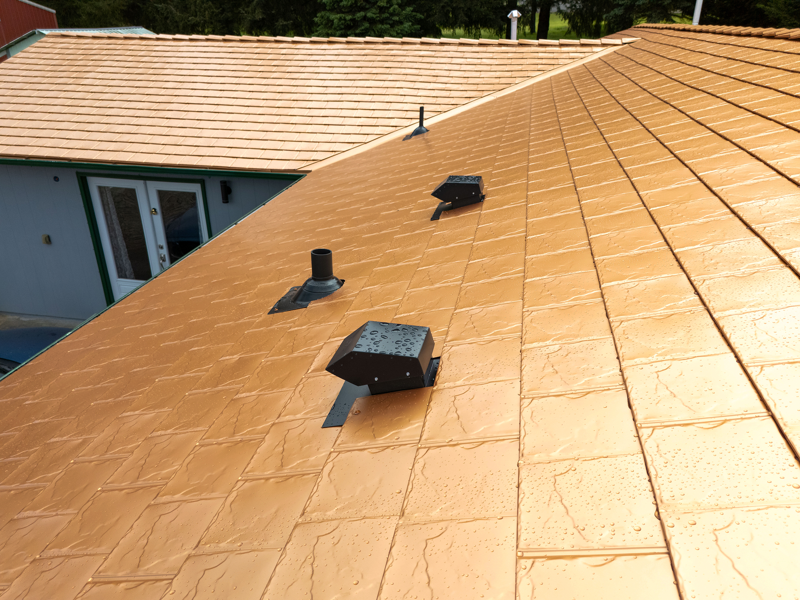 Close view of Interlock aluminum slate roof in Copper Penny finish with vent pipe and roof louvers, glistening with raindrops in Castle Rock, WA.