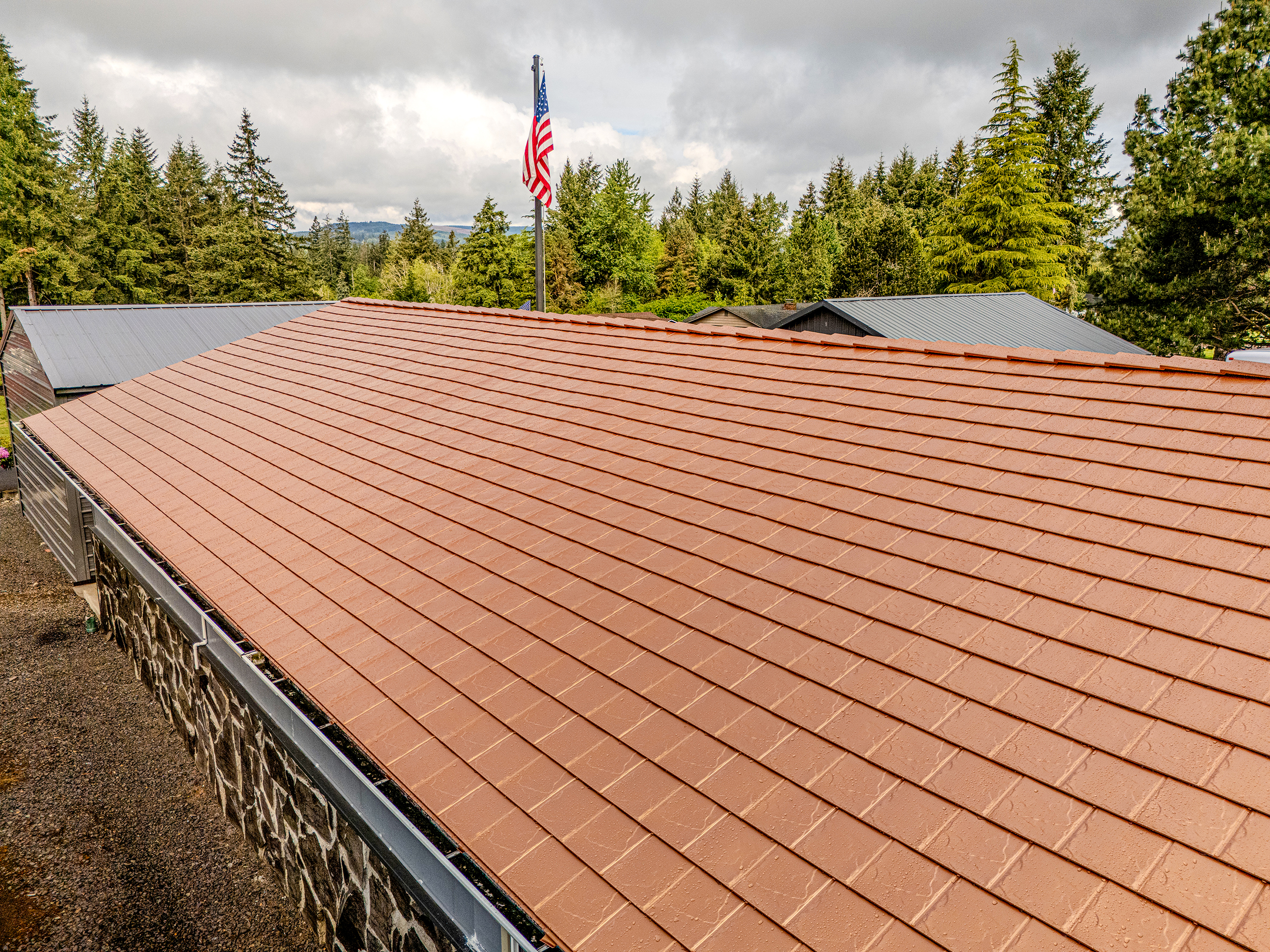 Aerial view of a ranch-style home with Interlock aluminum slate roof in Copper Penny on a stone-walled building surrounded by Pacific Northwest forest.