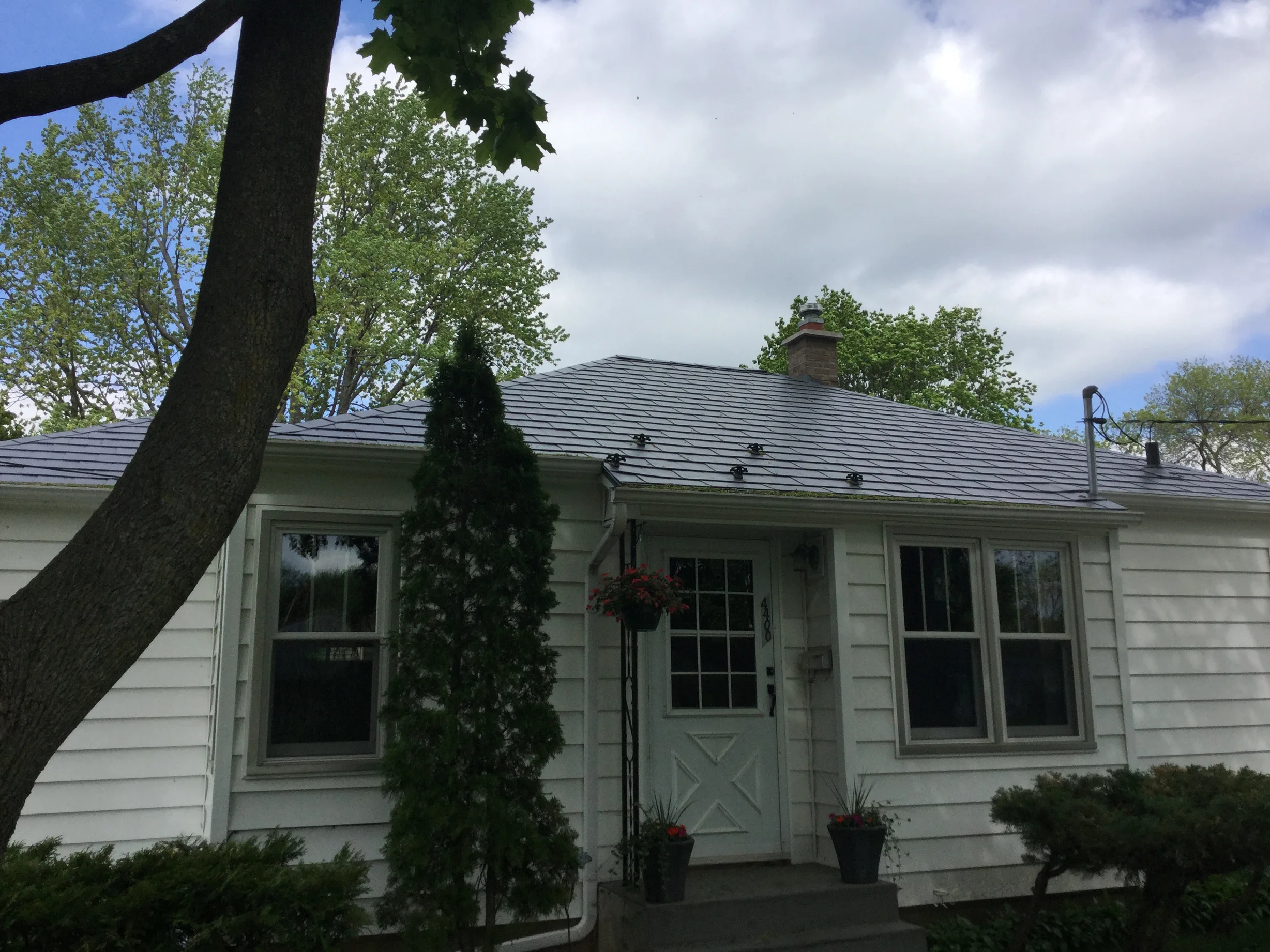 Charcoal Grey Interlock Slate aluminum roof on a white house with a metal roof among tall trees and bushes, Madison, Wisconsin