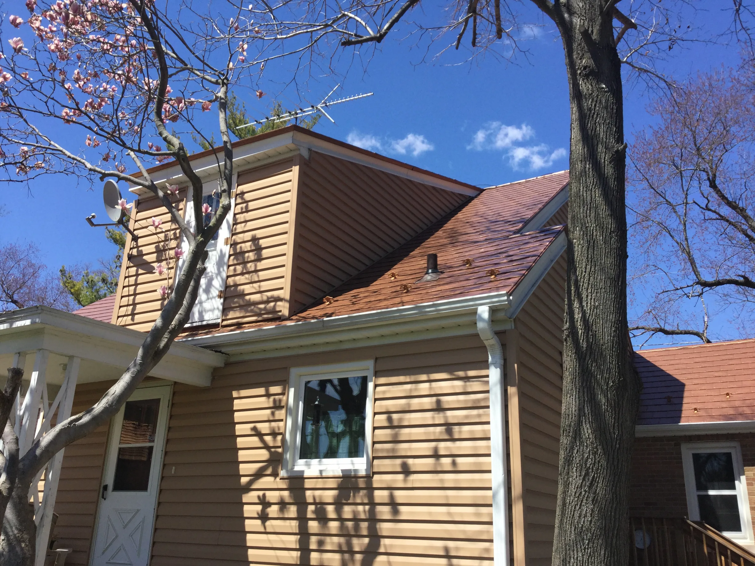 Aged Copper Interlock Slate aluminum roof on a brown one-storey home with a gable roof among tall pines, Watertown, Wisconsin