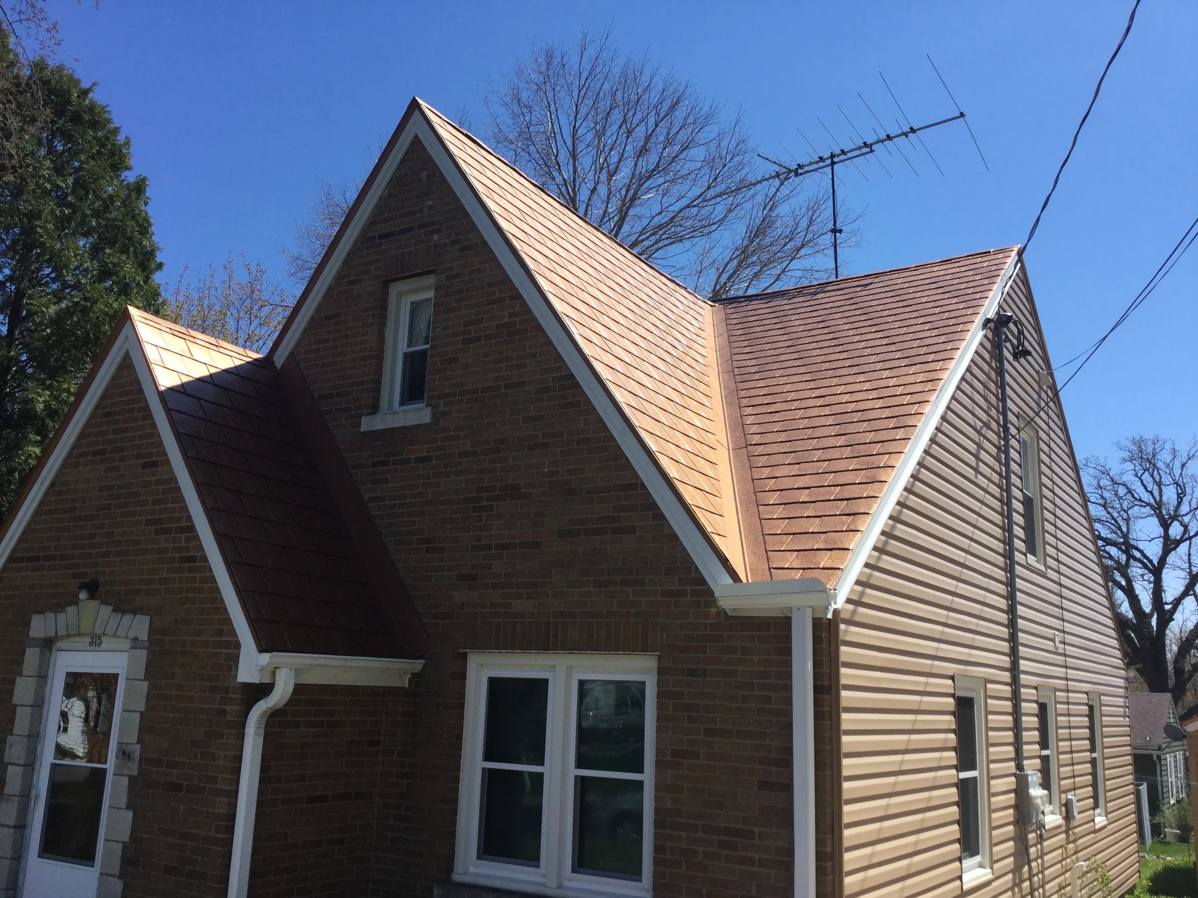 Aged Copper Interlock Slate aluminum roof on a brown house with a metal roof among trees, Watertown, Wisconsin