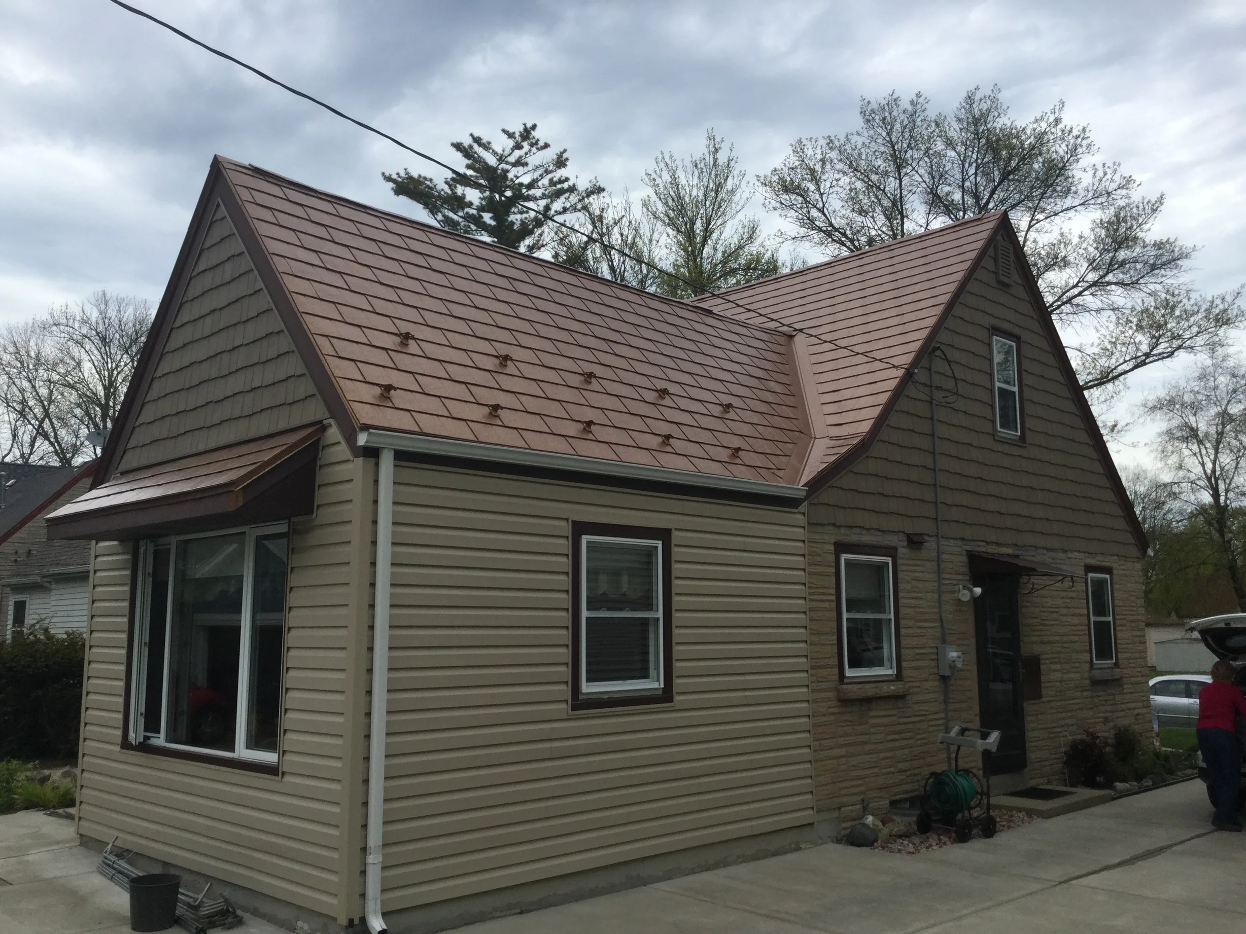 Aged Copper Interlock Slate aluminum roof on a brown Cape Cod home with dormers among tall trees, Milwaukee, Wisconsin
