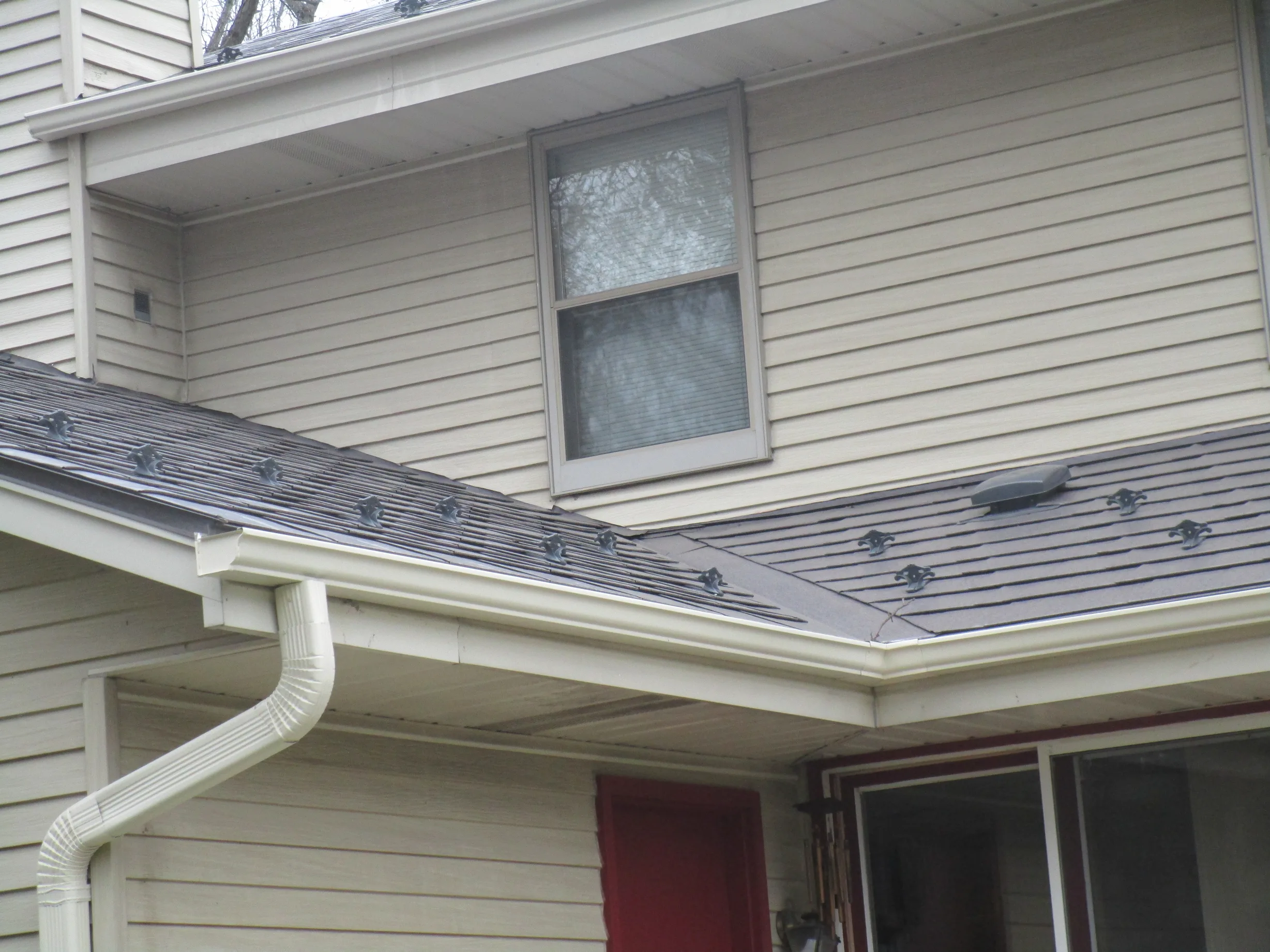 Tudor Brown Interlock Slate aluminum roof on a cream two-storey home with dormers among tall trees, Delafield, Wisconsin