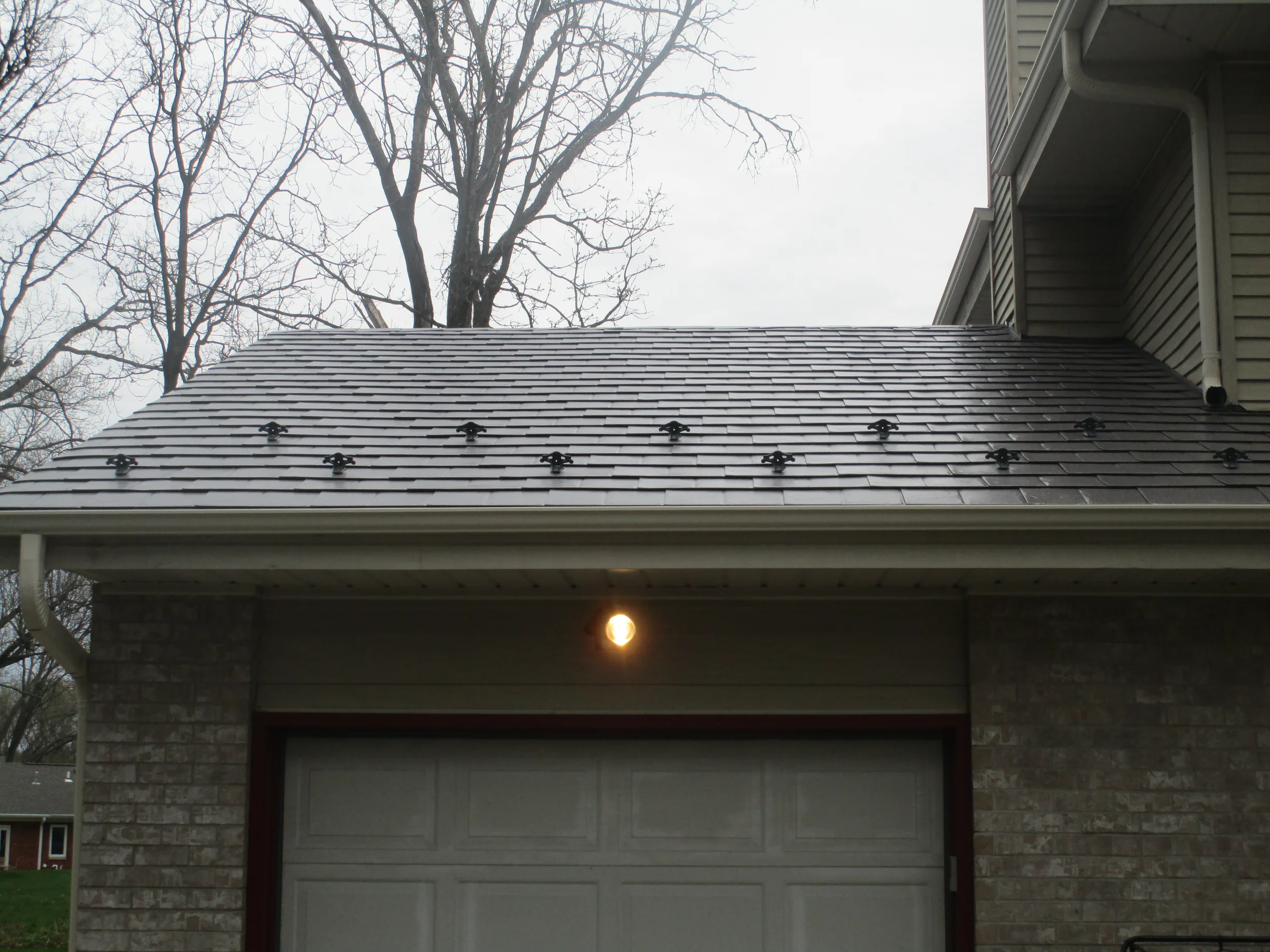 Tudor Brown Interlock Slate aluminum roof on a white Tudor home with dormers among tall pines, Delafield, Wisconsin