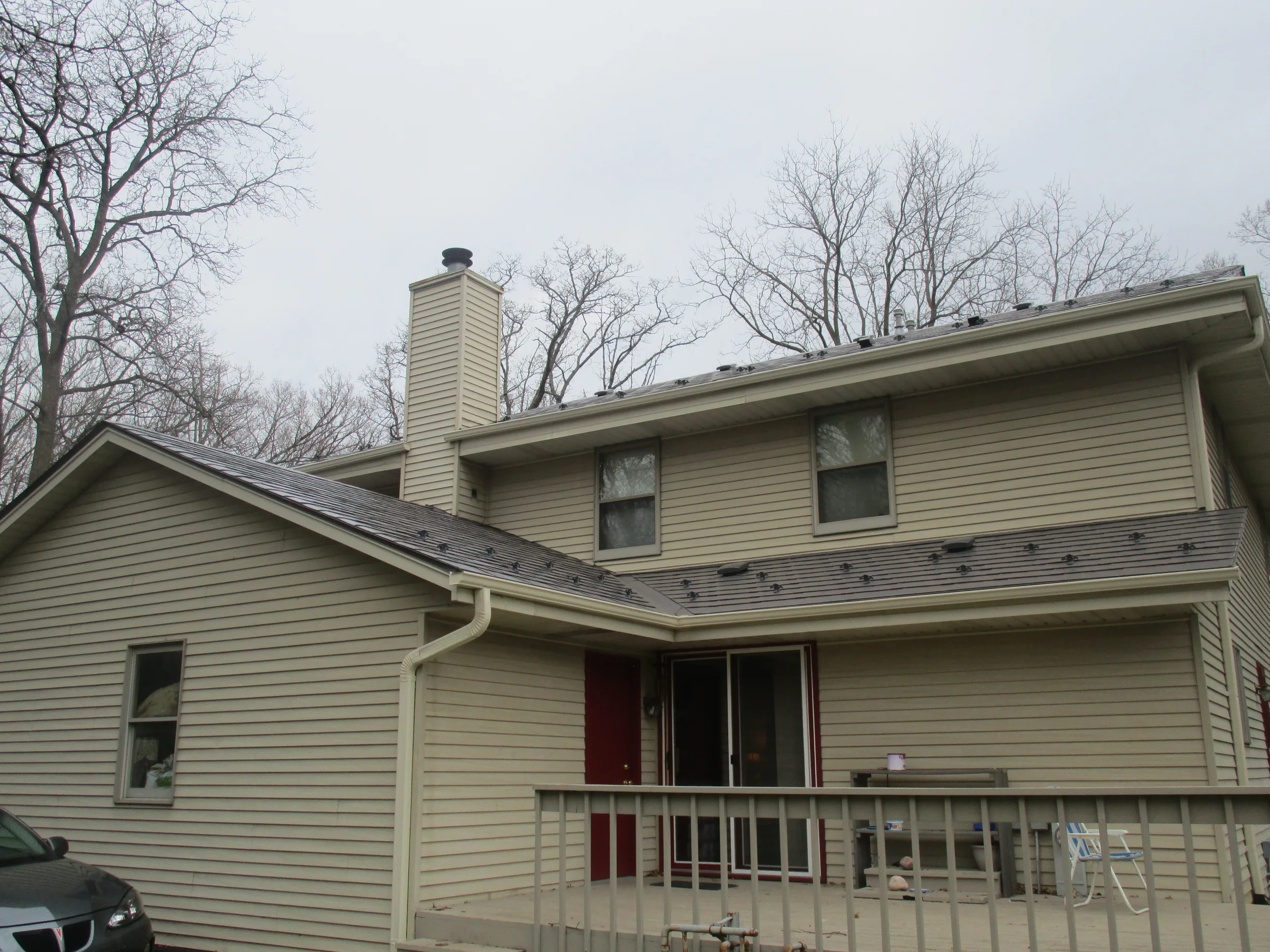 Tudor Brown Interlock Slate aluminum roof on a tan two-storey home with dormers among tall bare trees, Delafield, Wisconsin