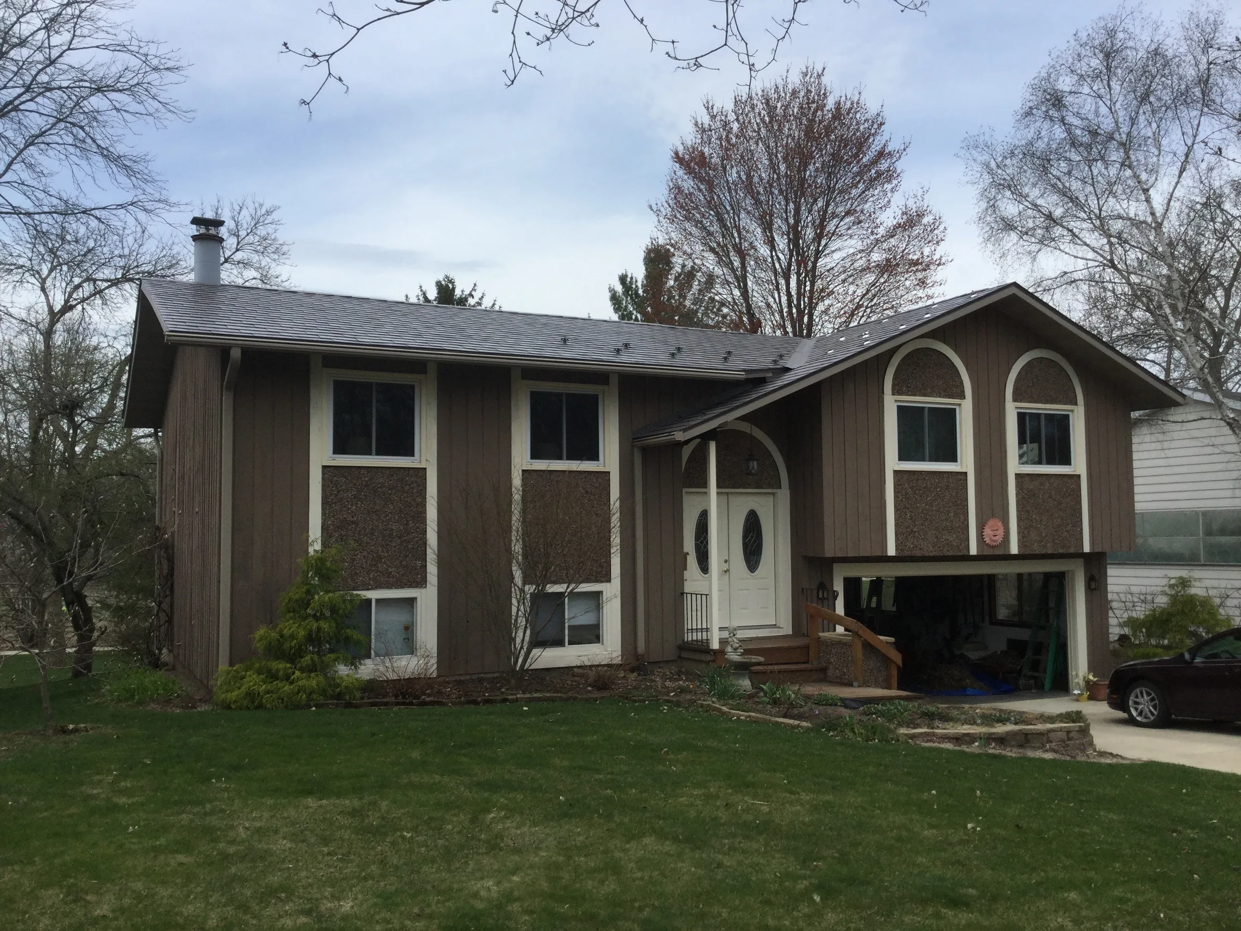 Weathered Interlock Slate aluminum roof on a brown single-storey home with a metal roof among tall, Madison, Wisconsin